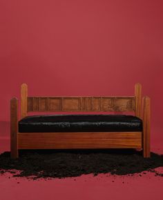 a wooden bench with black leather cushion against a red wall and dirt on the ground