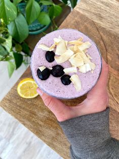 a person holding up a smoothie with blueberries and lemon wedges on top