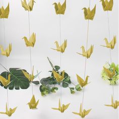 some yellow origami birds are hanging from the strings next to plants and flowers