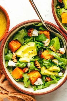 two bowls filled with salad on top of a white table next to oranges and other food