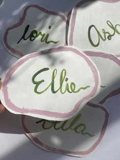 someone holding up four personalized coasters with green ink on them, in front of a white background