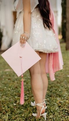 a woman in white dress holding a pink piece of paper with a tassel on it