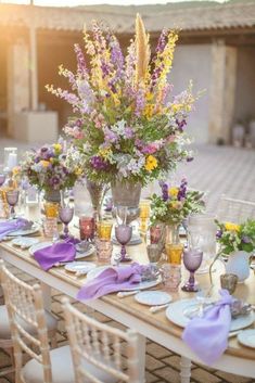 the table is set with purple and yellow flowers in vases, plates and napkins