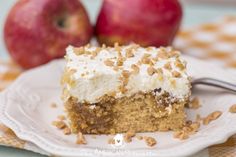 a piece of cake with white frosting and nuts on top sits on a plate next to two apples