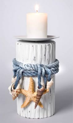 a candle that is sitting on top of a wooden pillar with shells and rope around it