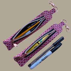 two pencils, pens and scissors are sitting on a pink fabric bag with zippered handles