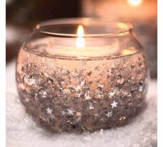 a candle that is sitting in the snow with stars on it's glass bowl