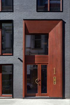 an entrance to a building with wooden doors and windows on both sides, in front of a brick wall