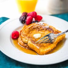 french toast with butter and syrup on a plate next to raspberries and orange juice