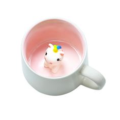 a white coffee cup with a small toy in it's center, inside which is filled with pink liquid