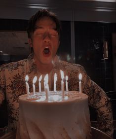 a man blowing out candles on a cake in front of his face with one eye open