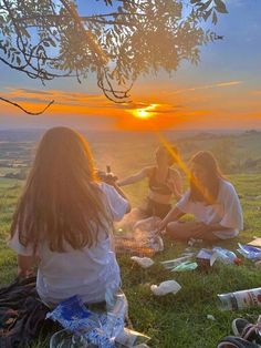 three women sitting on the grass at sunset with bottles and cans in their hands,