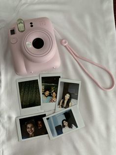 a pink camera sitting on top of a bed next to four polaroid pictures and a cord