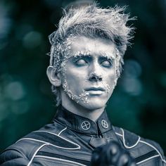 a man with white paint on his face and hair is pointing to the side while wearing black gloves