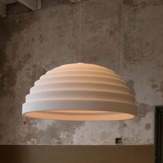 a white light hanging from the ceiling in a room with concrete walls and exposed ceilings