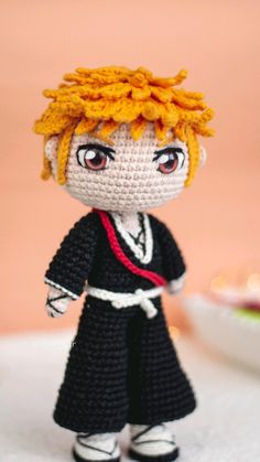 a crocheted doll with orange hair and black dress standing in front of a plate