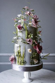 a three tiered cake with flowers on it sitting on a table in front of a gray wall