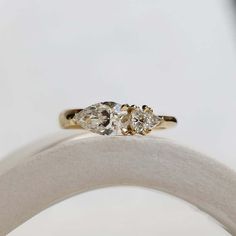 two pear shaped diamond engagement rings sitting on top of a white cloth ring holder in front of a white background