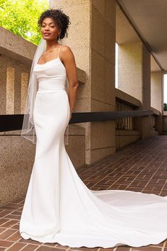 a woman in a white wedding dress standing next to a wall with her hands on her hips