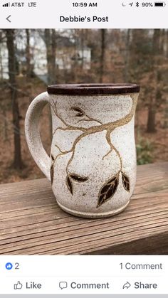 a coffee mug with leaves on it sitting on top of a wooden table in the woods