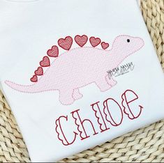 a white t - shirt with a pink dinosaur and hearts on the front that says born