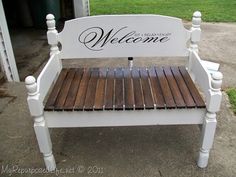 a white bench with wooden slats and welcome sign painted on the back, sitting in front of a house