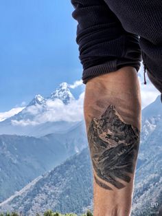 a man with a mountain tattoo on his leg is standing in front of the mountains