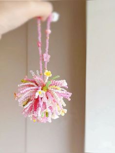 a hand holding a beaded necklace with flowers on the end and beads hanging from it