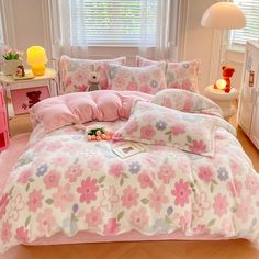 a bed with pink and green flowers on it in a bedroom next to a window