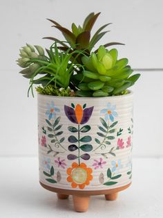 a potted plant with succulents and leaves painted on the outside is sitting on a wooden stand