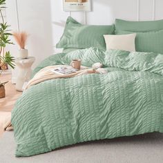 a bed with green comforter and pillows in a room next to a potted plant