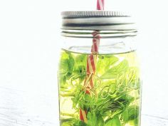 a mason jar filled with green leaves and straws next to a red striped straw