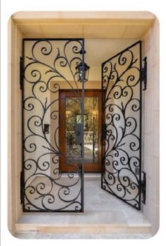 an ornate iron gate is open to reveal a foyer area with a door leading into it