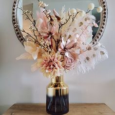 a vase filled with flowers on top of a wooden table next to a round mirror