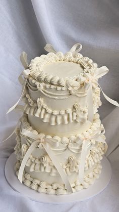 three tiered wedding cake with white ribbons and bows on top, sitting on a plate