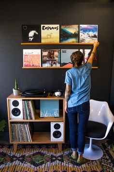 a woman standing in front of a desk with records on the wall and shelves above it