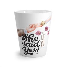 a white cup with the words she said yes on it and purple flowers in front