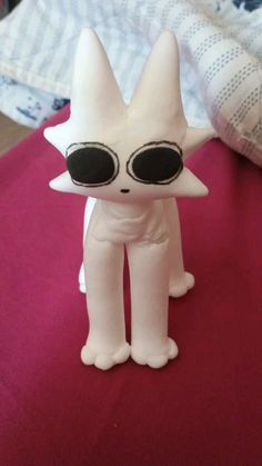 a white cat toy with large round glasses on it's face and legs, sitting on a bed