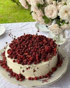 a white cake with strawberries on it sitting on a table next to some flowers