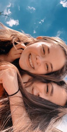 two young women are smiling and posing for the camera with their hair blowing in the wind