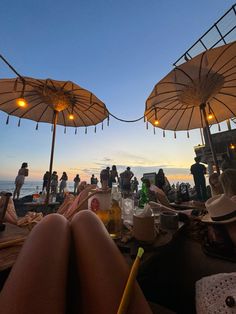 people are sitting under umbrellas on the beach at sunset or sunrise, with drinks in front of them