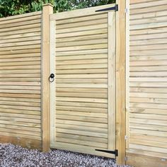 a wooden fence with two doors on each side and gravel in the foreground next to it