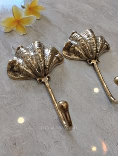 two decorative brass scallop hooks on a marble surface with flowers in the background