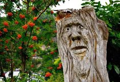 a tree stump with a face carved into it's trunk and surrounded by flowers