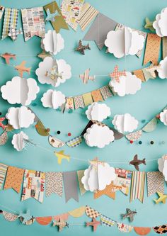 paper airplanes and clouds are hanging from a string on a blue wall with other decorations