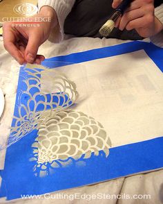 a person is cutting out some paper on a piece of blue and white material with a paintbrush