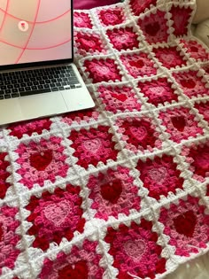 an open laptop computer sitting on top of a pink and white crocheted blanket