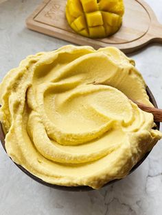 a bowl filled with yellow custard next to a wooden spoon and cutting board