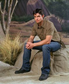 a young man sitting on top of a rock next to a tree and grass area