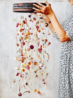 a woman holding a tray with flowers hanging from it's sides, in front of a wall